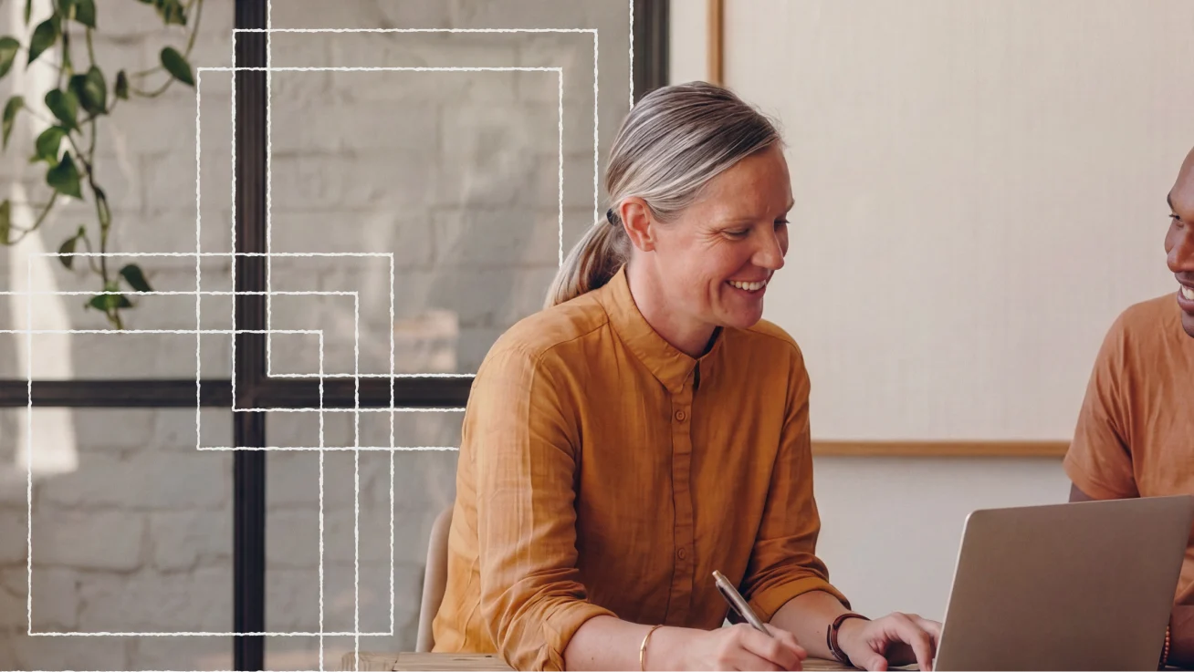 Two colleagues smiling while reviewing work on a laptop.