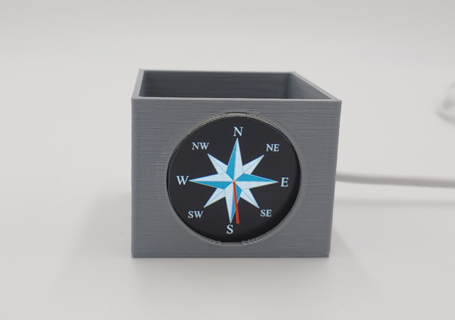 GC9A01A round display in a 3D printed box showing a compass rose and north, east, south, west heading lables. A red pointer needle points towards south.