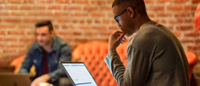 A man working on the laptop and sitting around peoplw